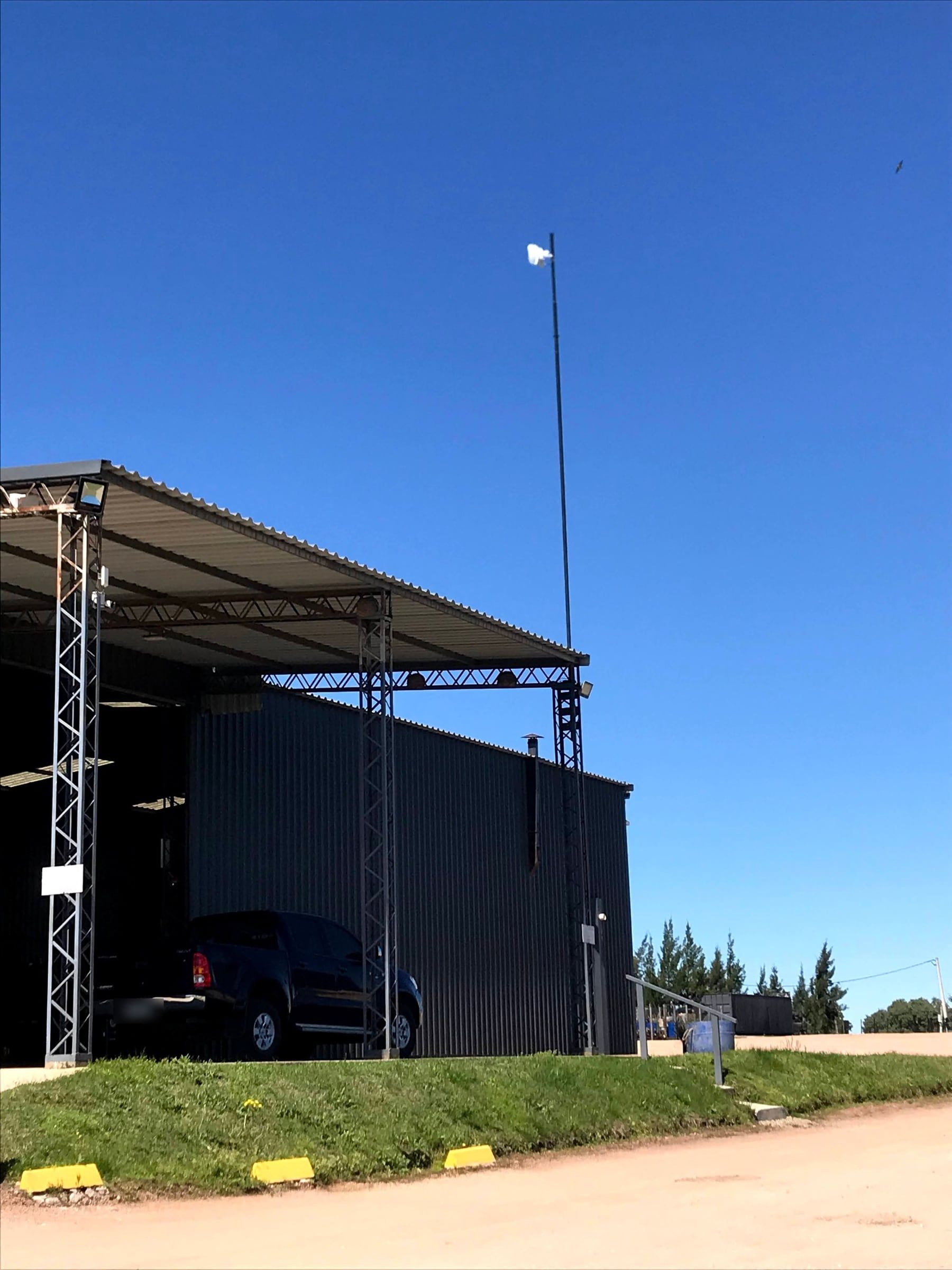 Mast-mounted radio rising above an industrial shed, positioned for line of sight over the surrounding structures.